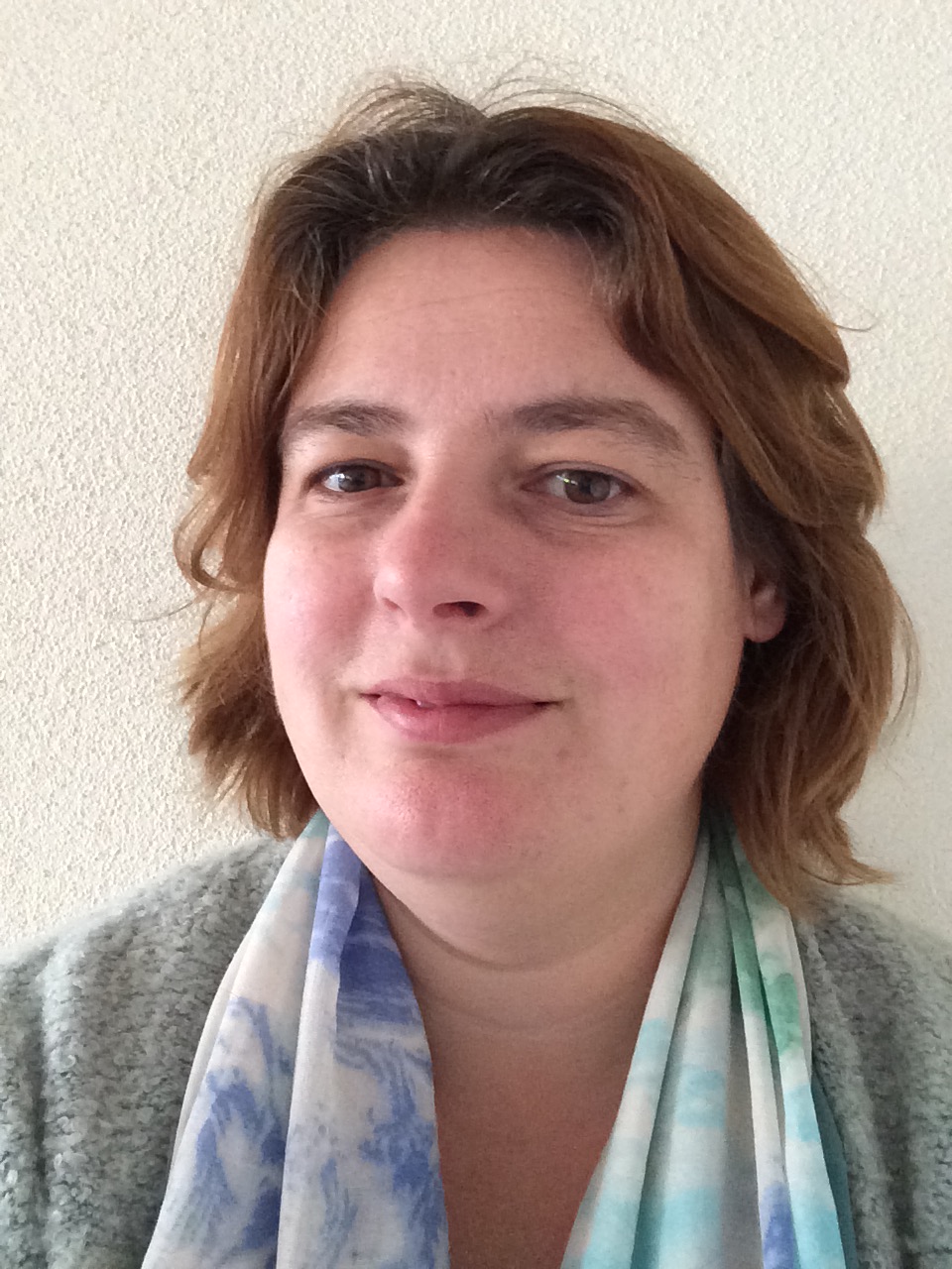 Portretfoto een vrouw met halflang donkerblond haar met een vriendelijke uitdrukking, tegen een lichte achtergrond.